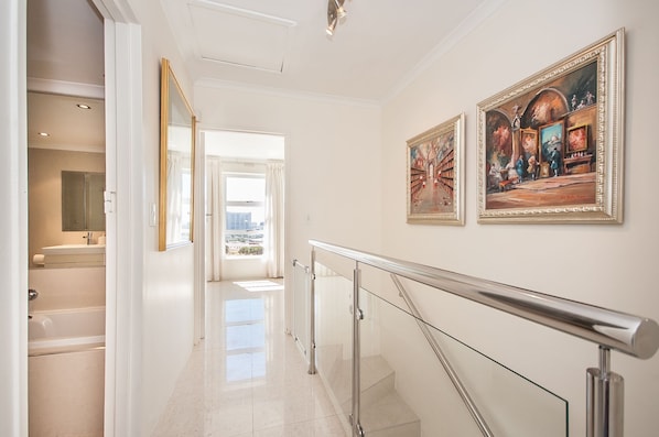 A hallway with a glass railing, a view of a bathroom, and two framed paintings on the wall. - 3 Canterbury Square (Cape Town)