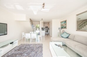 Un salon moderne avec une table basse en verre, un canapé et un coin repas avec des chaises blanches.