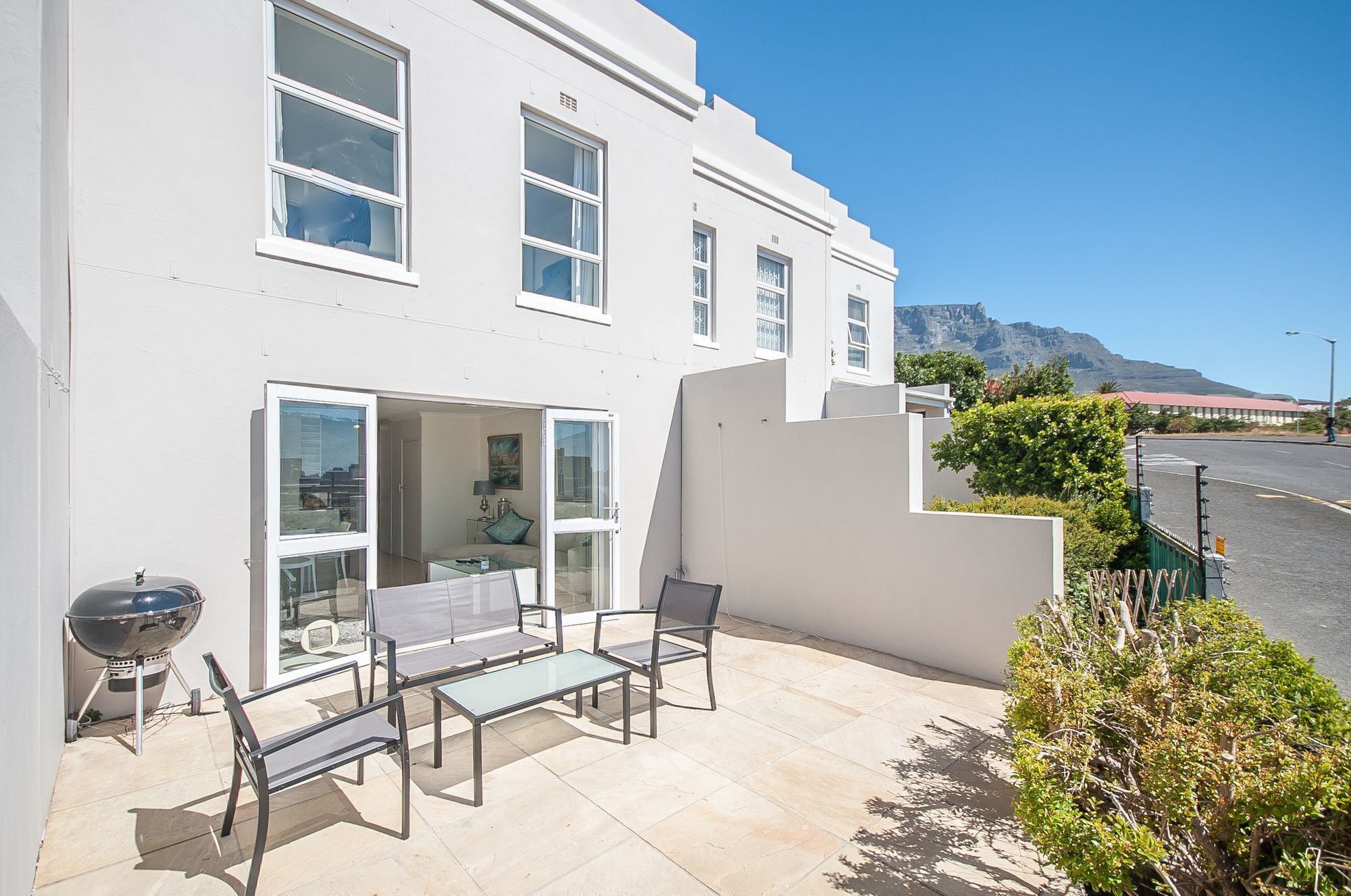 A modern white building with a patio area featuring a grill, seating, and a view of a mountain.