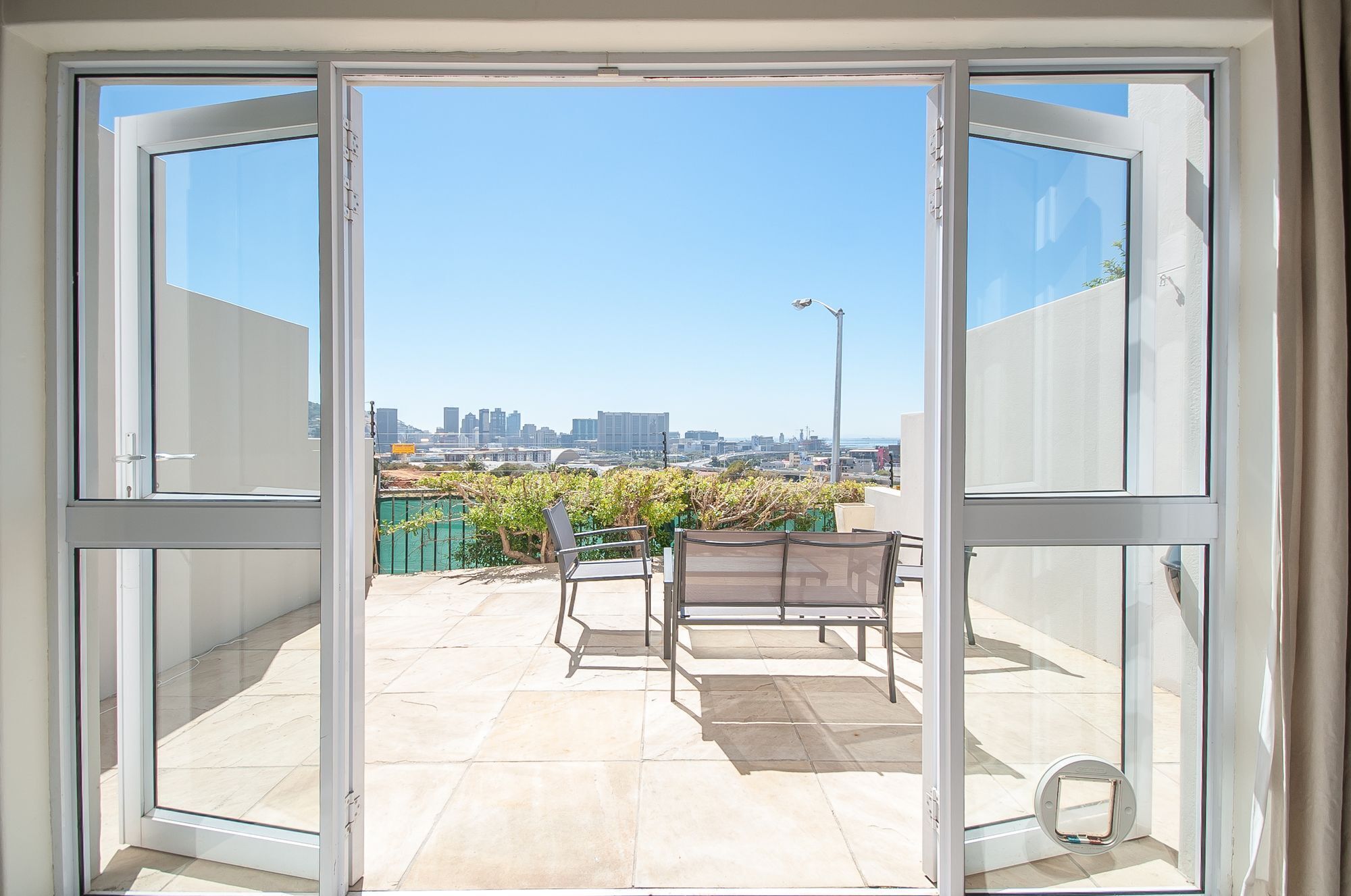 A view through a glass door to an outdoor patio area with a cityscape in the background.