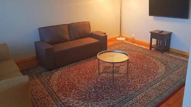 A living room with a sofa, a small round table, a floor lamp, and a TV on the wall. - Bramber Court (Cape Town)
