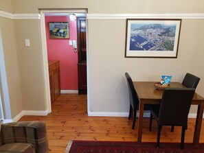 A dining area with a wooden table and chairs, a framed cityscape picture, and a red rug. - Bramber Court (Cape Town)