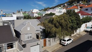 A residential street with houses, a white car parked on the side, and a hill in the background. - Bramber Court (Cape Town)