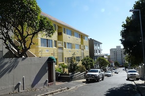 A multi-story residential building with a yellow facade, balconies, and a clear sky. - Bramber Court (Cape Town)