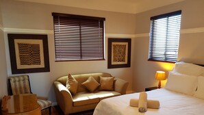 A hotel room with a bed, a sofa, a chair, and two windows with blinds. - Bramber Court (Cape Town)