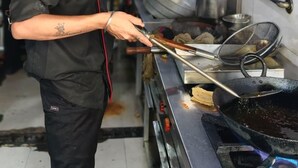 Un chef dans une cuisine professionnelle équipée d’appareils en acier inoxydable, d’un grand wok et d’ustensiles de cuisine.