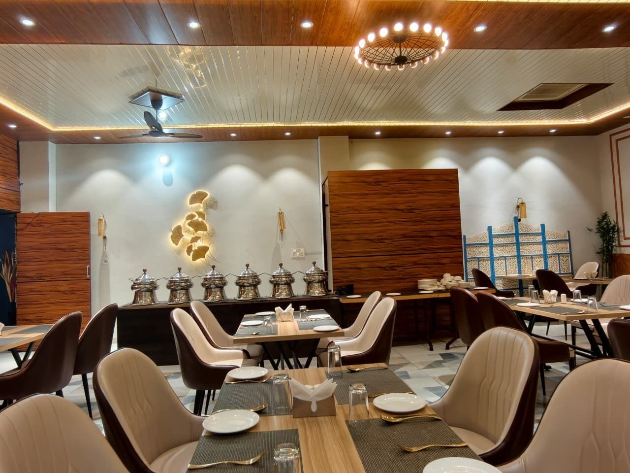 A dining area with multiple tables and chairs, a decorative wall with a light fixture, and a ceiling with recessed lighting.