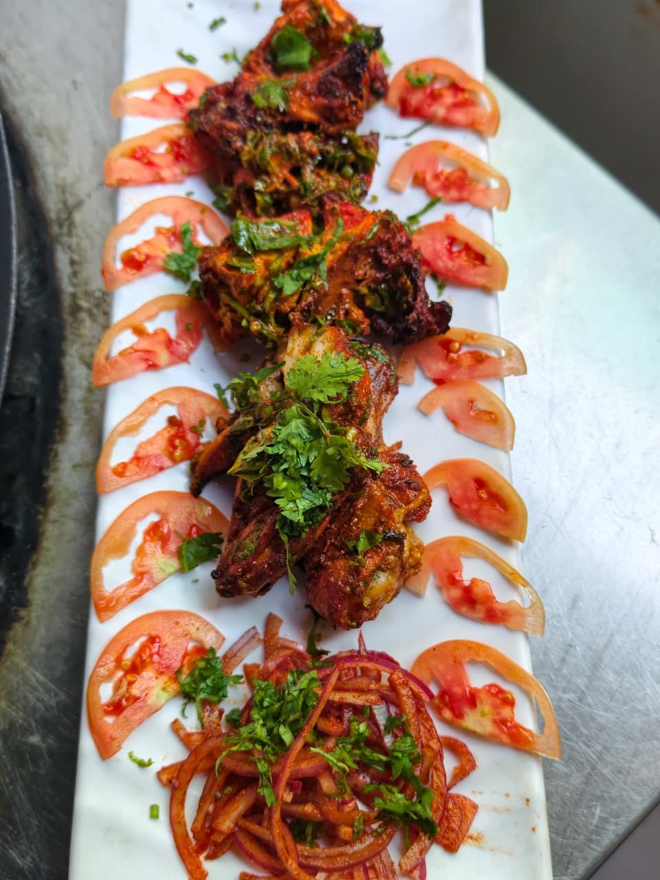 A white rectangular plate with grilled chicken wings, tomato slices, and onion rings.