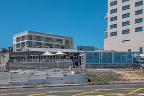Un edificio frente al mar con varios balcones, una estructura de vidrio y zonas de estar al aire libre.