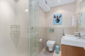Un baño moderno con cabina de ducha de vidrio, inodoro, lavamanos y toallero.
