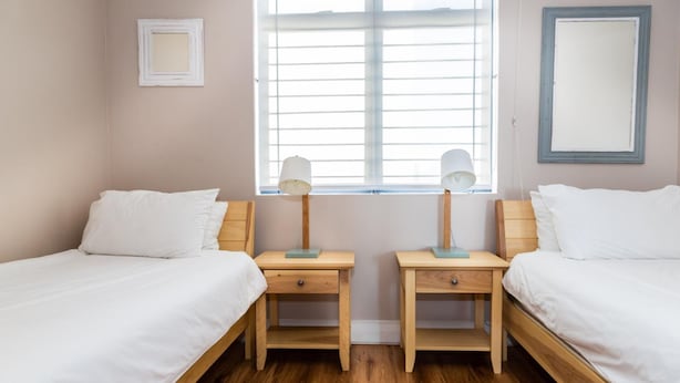 A room with two single beds, wooden nightstands, a window with blinds, and a mirror on the wall. - 236 Eden On the Bay (Cape Town)