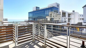 A modern building with a glass facade, a metal railing, and a view of the sea. - 236 Eden On the Bay (Cape Town)