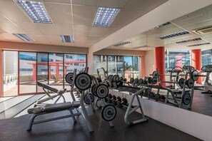 A gym with weightlifting equipment, large windows, and a view of buildings outside. - The Icon by ITC Hospitality (Cape Town)