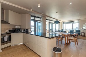 A modern kitchen with white cabinets, a black countertop, and a dining area with wooden chairs and a table. - The Icon by ITC Hospitality (Cape Town)