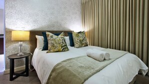 Habitación de hotel con una cama, una mesita de noche, una lámpara y una ventana con cortinas.
