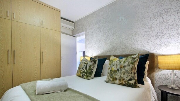 Habitación de hotel con cama, armario y mesita de noche con lámpara.