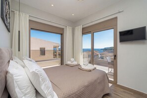 Ein modernes Hotelzimmer mit einem großen Bett, zwei Fenstern mit Vorhängen, einem Flachbildfernseher und Blick aufs Meer.