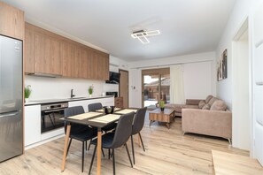 Eine moderne Küche mit Holzschränken, ein Essbereich mit Tisch und Stühlen sowie ein Wohnzimmer mit einer Couch.
