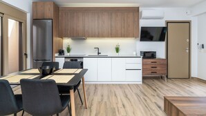 Moderni keittiö, jossa on puiset kaapit, ruostumattomasta teräksestä valmistettu jääkaappi, mikroaaltouuni sekä ruokailutila, jossa on pöytä ja tuolit.