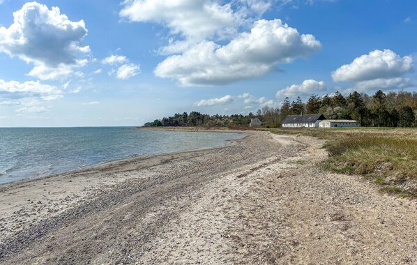 A beach with pebbles, a house, and trees in the background. - 2 bedroom beautiful home in øster assels (Øster Assels)