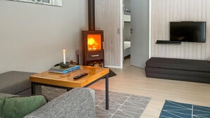 A cozy living room with a wood-burning stove, a sofa, a coffee table with books and a remote, and a TV mounted on the wall. - 2 bedroom beautiful home in øster assels (Øster Assels)