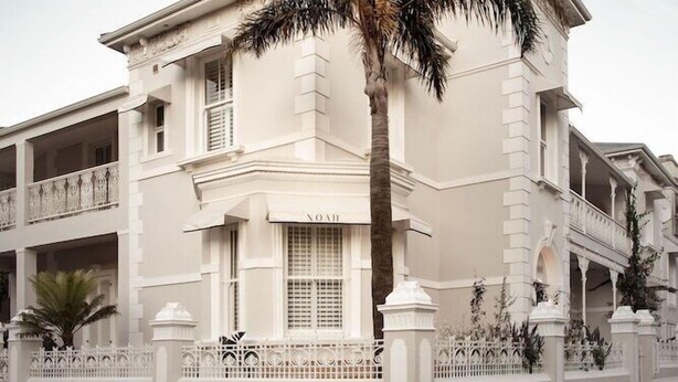 A white colonial-style building with a central entrance, balconies, and a palm tree in front. - Underberg House (Cape Town)