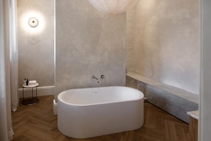 A modern bathroom with a freestanding bathtub, a small round table with toiletries, and a wall-mounted light fixture. - Underberg House (Cape Town)