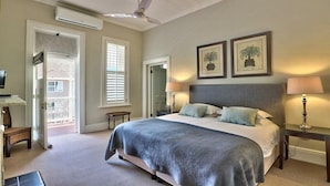 A bedroom with a large bed, two bedside lamps, a ceiling fan, and two framed pictures on the wall. - Underberg House (Cape Town)