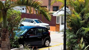 Un edificio residencial con balcón, coches aparcados y plantas en macetas.