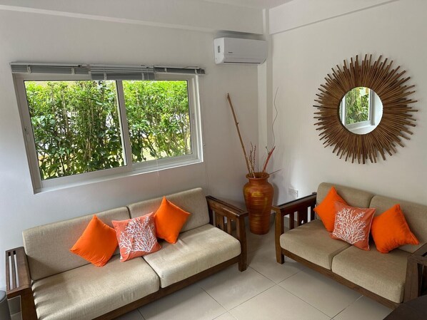 Una sala de estar con dos sofás, un ventanal con vista a la vegetación, un espejo en la pared y un jarrón decorativo.