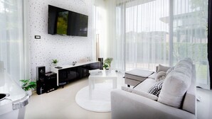 Una sala de estar moderna con un televisor de pantalla plana montado en una pared con textura, un sofá blanco y una mesa de centro.
