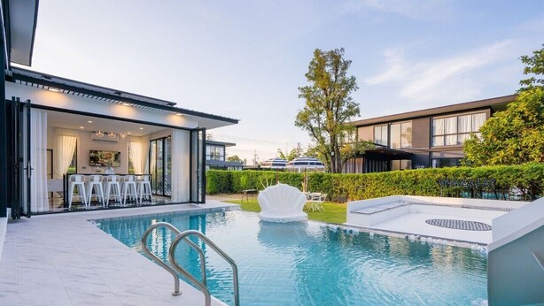 Un área de piscina moderna con vista despejada, una zona de estar con sillas y un seto bien cuidado.