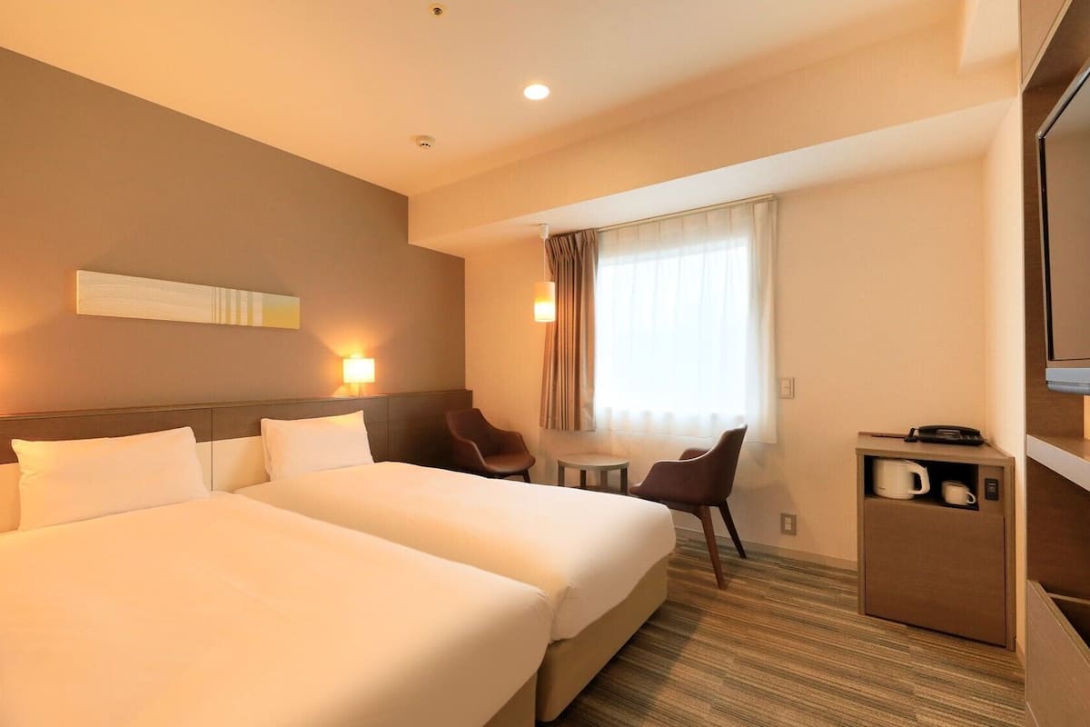 Ein Hotelzimmer mit zwei Betten, einem Schreibtisch, einem Sessel, einem Fernseher und einer Kaffeemaschine.