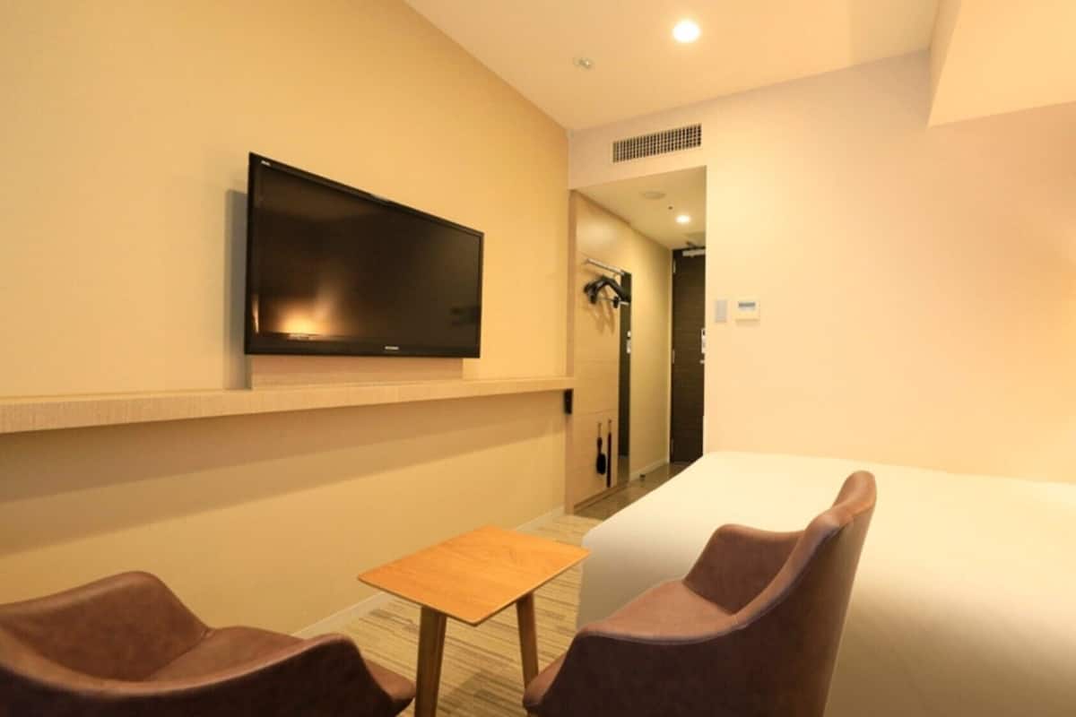 Ein Hotelzimmer mit Bett, Wandfernseher, kleinem Tisch, zwei Stühlen und einer Lampe.