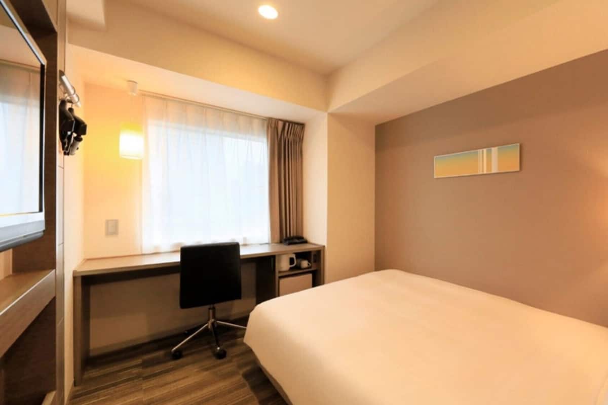 Ein Hotelzimmer mit Bett, Schreibtisch, Stuhl und einem Fenster mit Vorhängen.