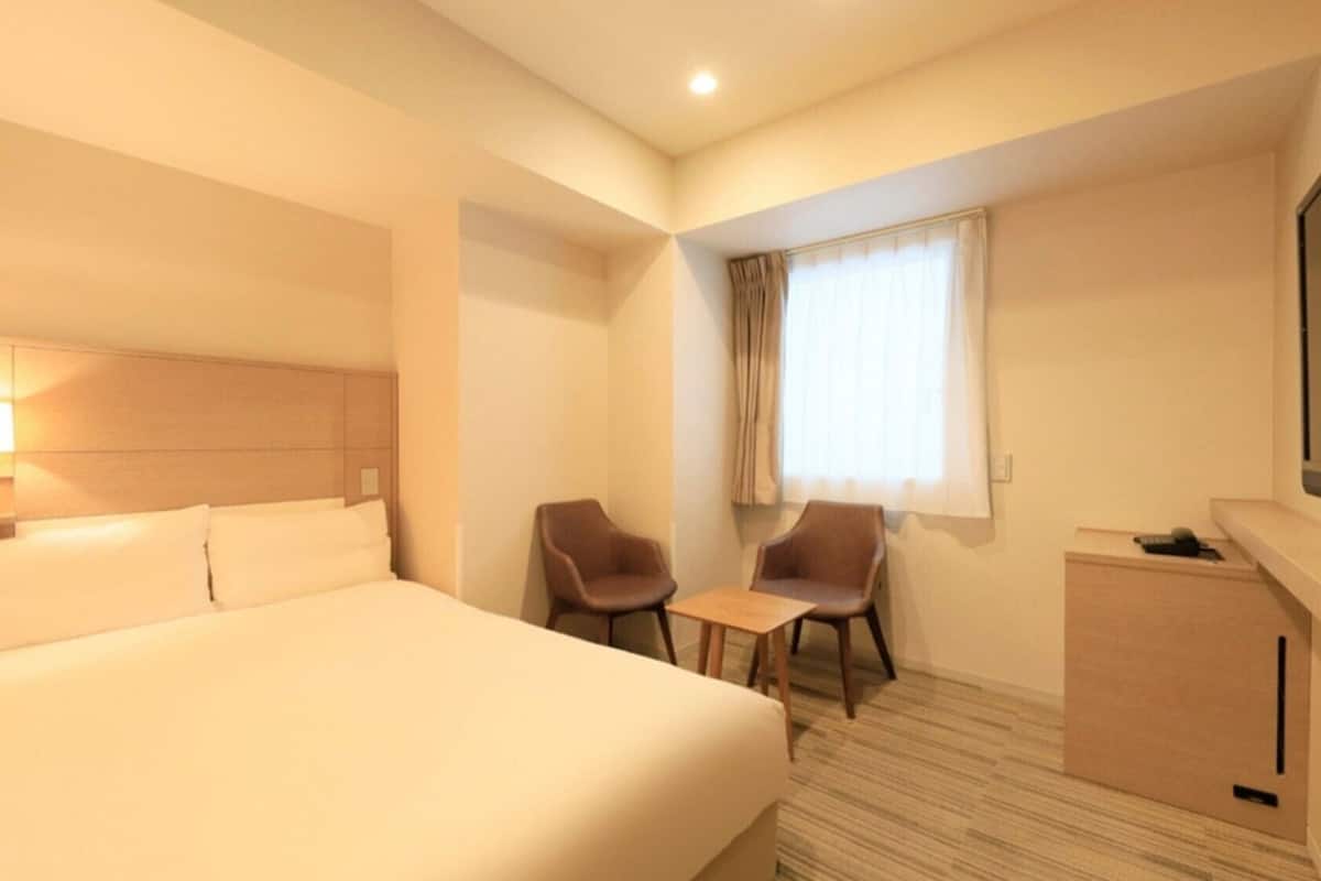 Ein Hotelzimmer mit Bett, Schreibtisch, zwei Stühlen, Fernseher und einem Fenster mit Vorhängen.