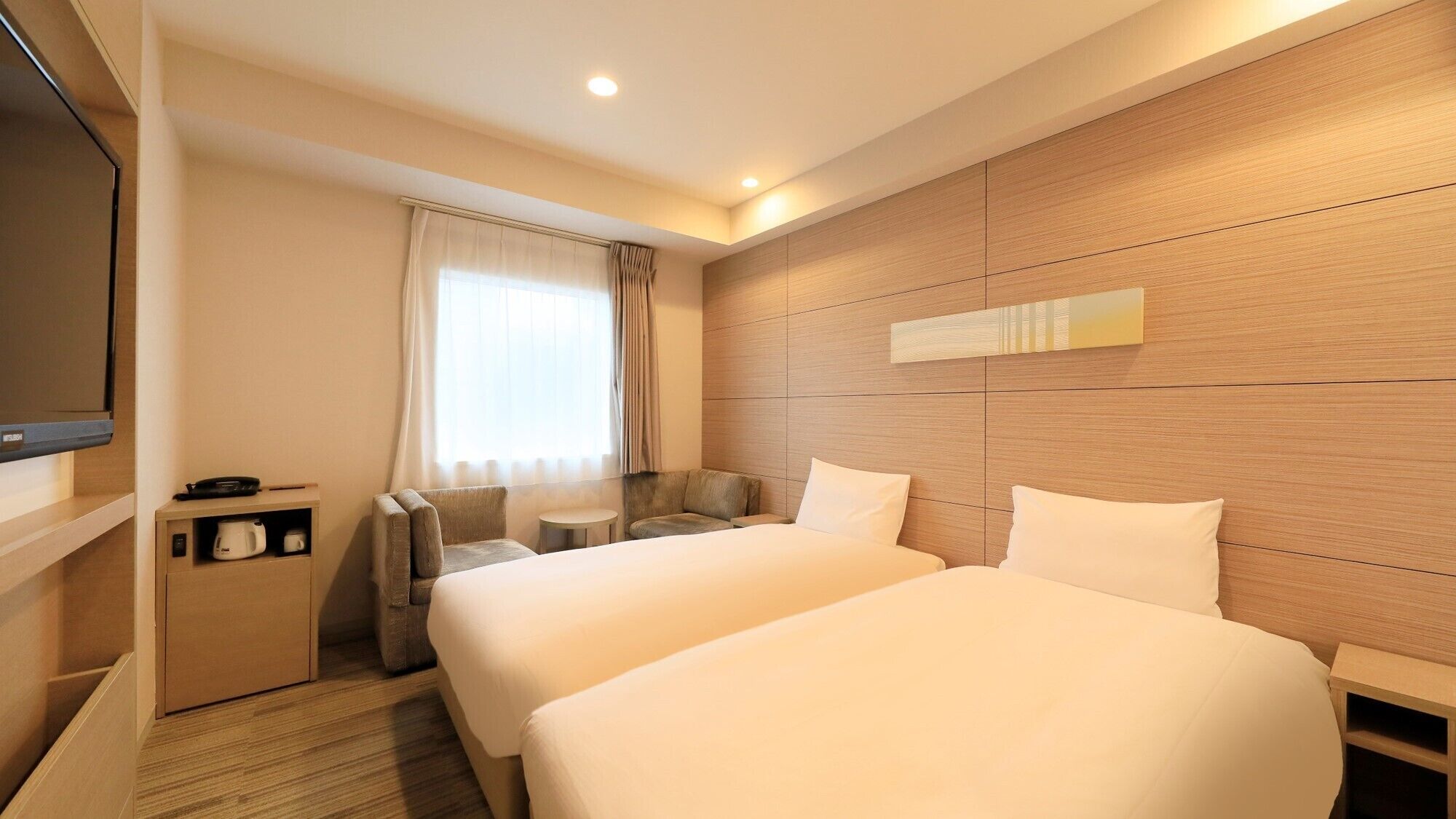 A hotel room with two beds, a TV, a coffee maker, and a window with curtains.