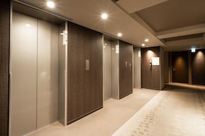 A hotel corridor with multiple elevators, carpeted flooring, and a wooden wall paneling. - Viainn Higashi Ginza (Tokyo)