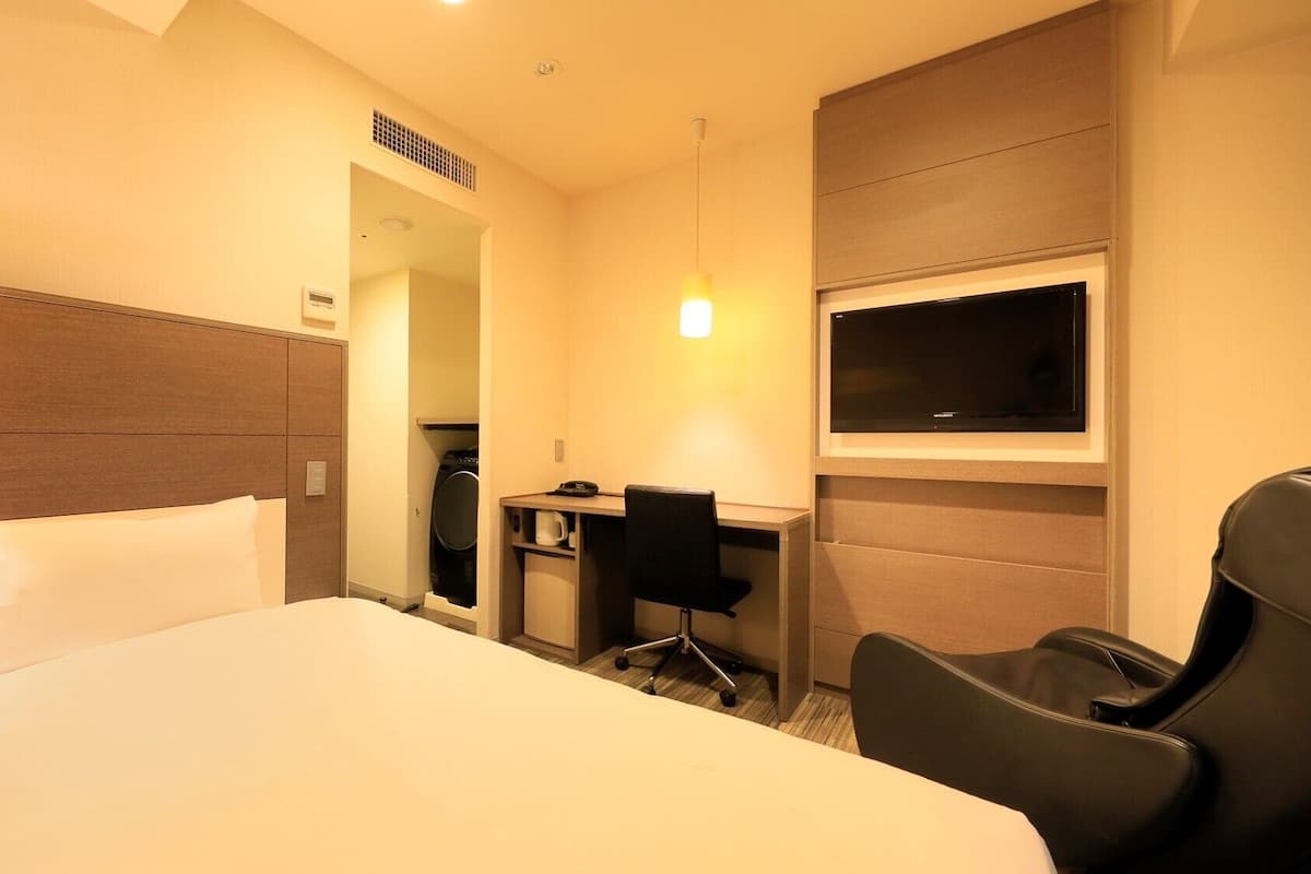 Ein Hotelzimmer mit Bett, Schreibtisch, Stuhl, Fernseher und einer kleinen Küchenzeile.