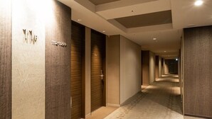 A modern hotel corridor with wooden paneling and a patterned carpet. - Viainn Higashi Ginza (Tokyo)