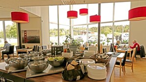 A buffet setup with various bowls and plates, a sign reading "OLJA & VINGE," and a view of the outside through large windows.