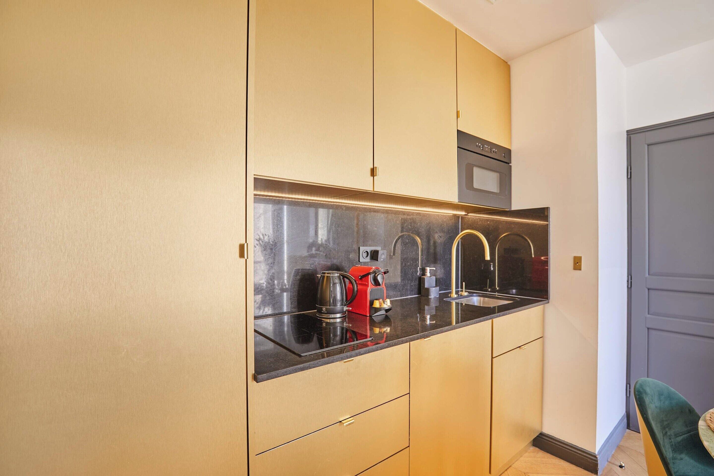 Una cocina compacta con encimera negra, electrodomésticos de acero inoxidable y armarios de madera.