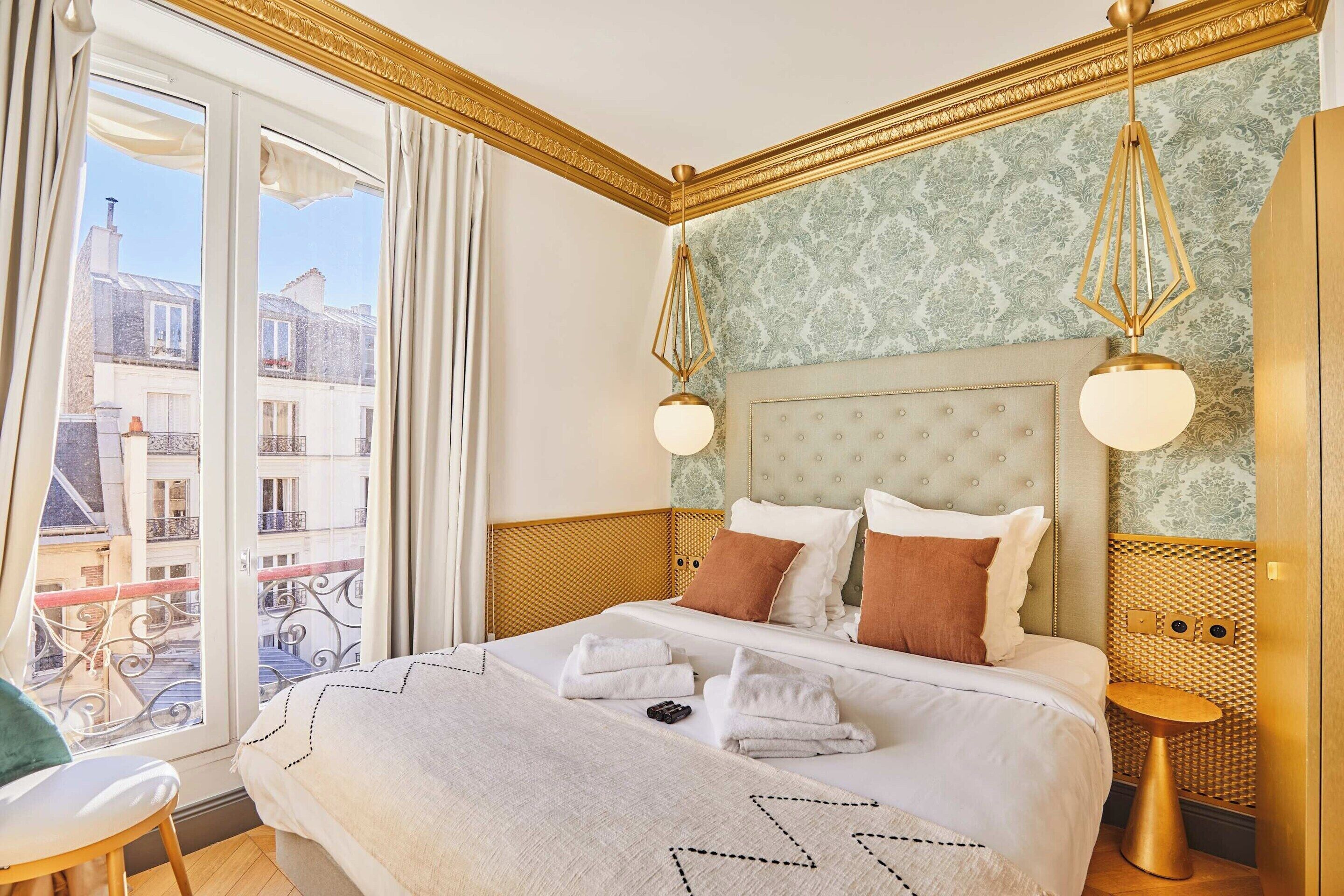 Een hotelkamer met een groot bed, een balkon met uitzicht op Parijse gebouwen, en een klassiek design met gouden accenten.