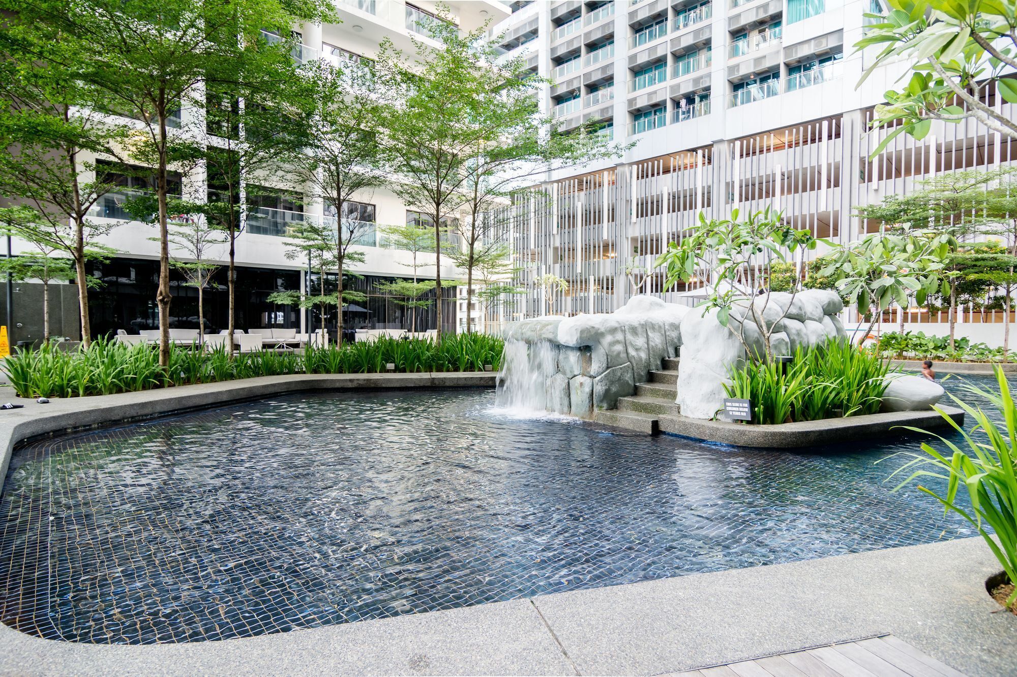 A modern indoor pool with a waterfall feature, surrounded by greenery and contemporary architecture.