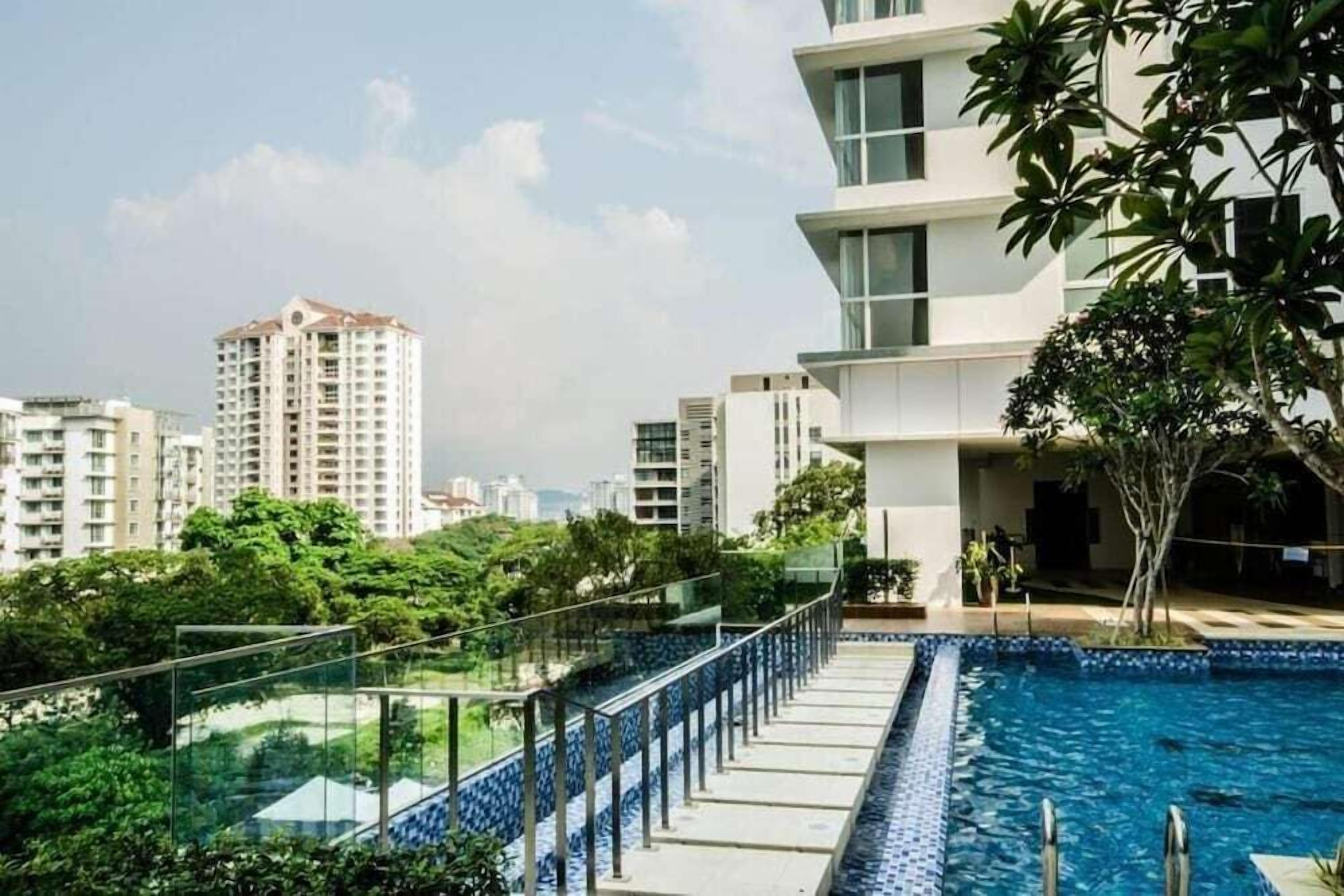 A modern building with a rooftop pool, surrounded by greenery and other high-rise buildings in the background.