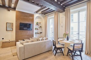 A living room with a sofa, a TV mounted on the wall, a dining table with chairs, and a balcony with curtains. - Charming Apartment in the Center of Paris (Paris)