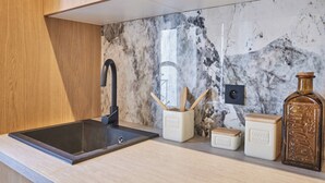 A kitchen with a black sink, wooden cabinets, a marble backsplash, and various kitchen items including a spice rack and containers. - Charming Apartment in the Center of Paris (Paris)