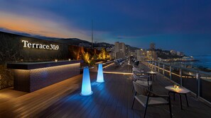 A terrace with a sign reading 'Terrace 30.9,' wooden flooring, lounge chairs, and tables with ambient lighting. - Village Atami (Atami)