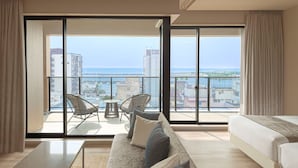 A modern hotel room with a balcony, a sofa, two chairs, and a view of the sea and cityscape. - Village Atami (Atami)