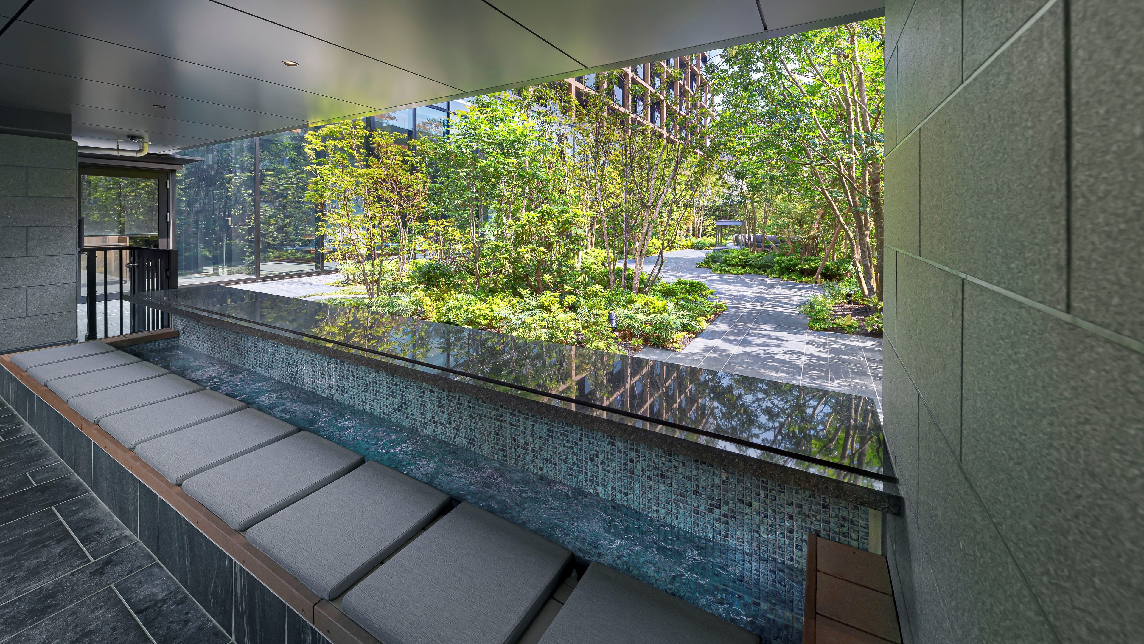 A modern indoor space with a glass barrier, a tiled floor, and a view of a landscaped garden.